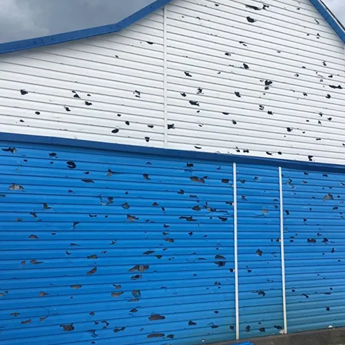 Close-up view of blue siding with visible hail damage, showing dents and texture.