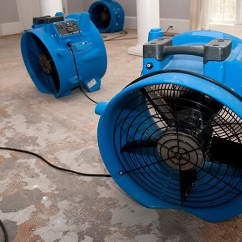 Various blue fans used for water restoration on a damp surface, demonstrating professional water damage mitigation and drying services.