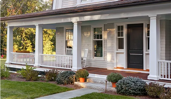 Charming home featuring a custom-built porch, highlighting professional deck construction services with stylish design and landscaping.