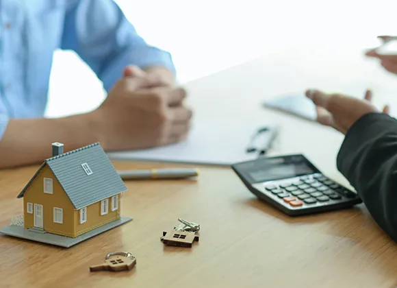 Hands reviewing insurance paperwork alongside a small model house on a table.