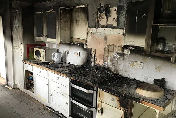 Interior of a kitchen showing fire damage with charred cabinets and blackened surfaces.