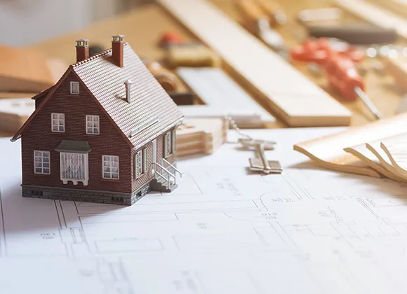 Model house placed on a table among paperwork and documents related to home reconstruction.