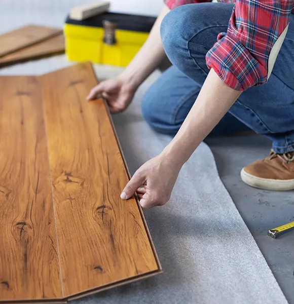 Close-up of a person adjusting wooden flooring with tools during installation.