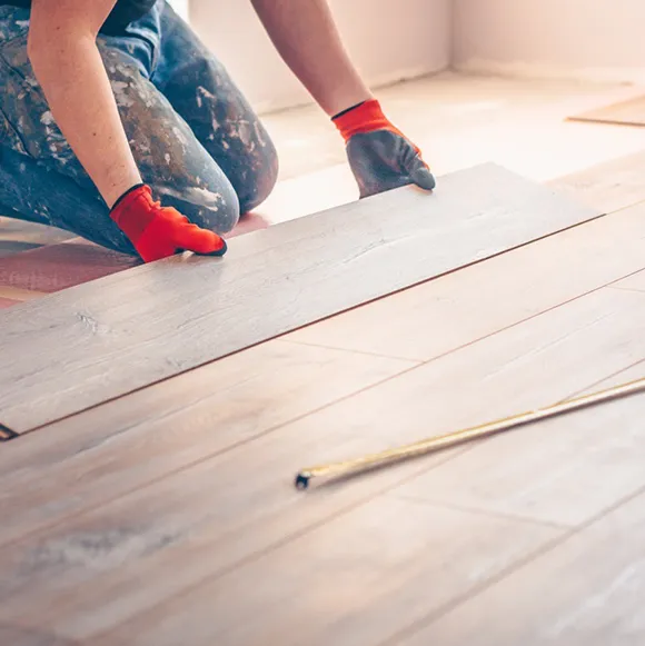 Person in gloves carefully laying down flooring material on a wooden surface.